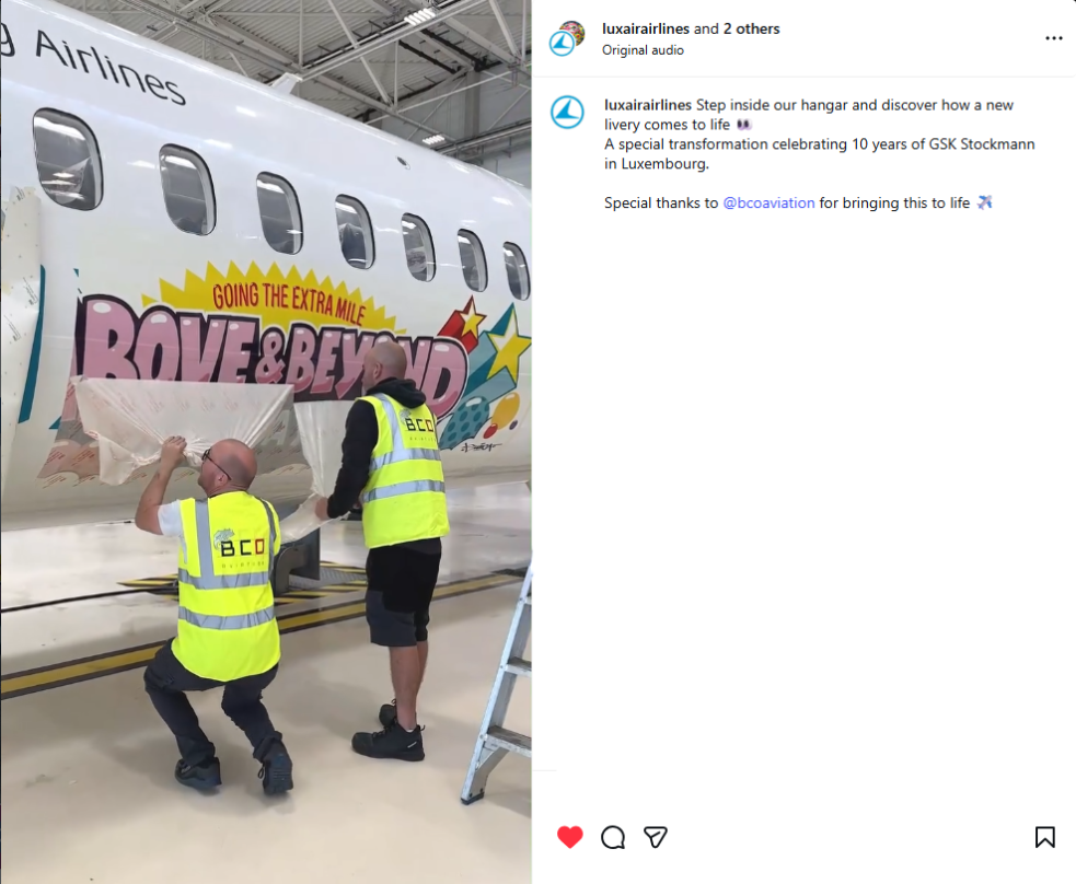 Photo of two workers applying the new anniversary livery wrap to the Luxair aircraft in the hangar