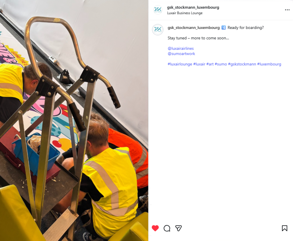 Photo of a worker fitting an anniversary-branded luggage cart in the Luxair Business Lounge